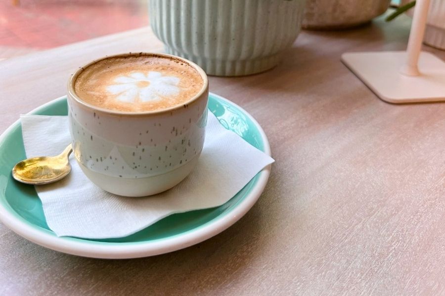 a cappuccino sits on a green plate next to a potted succulent