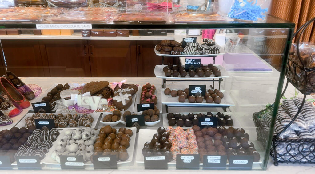 Close-up of assorted labeled chocolate truffles arranged in trays inside a glass display case.