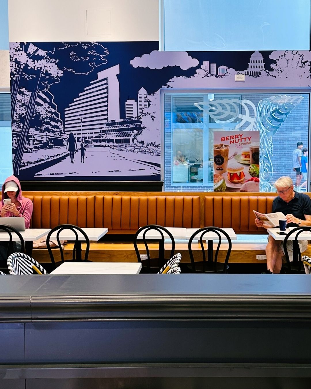 Long caramel-colored banquette seating with people reading at Paris Baguette bakery cafe in Bethesda
