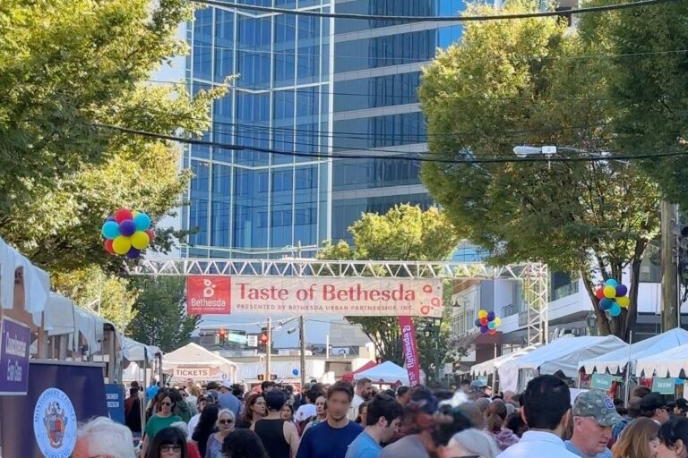 Wide view of crowd, white vendor tents, and colorful balloons lining downtown Bethesda street
