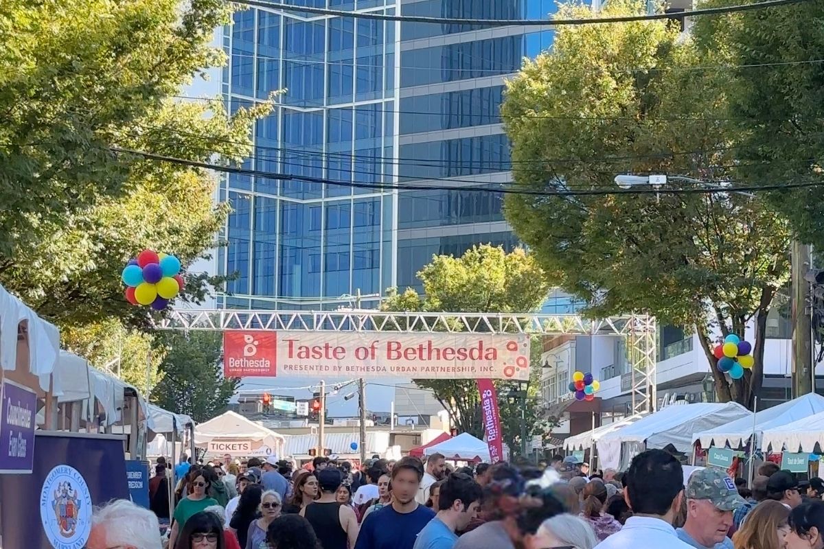 Wide view of crowd, white vendor tents, and colorful balloons lining downtown Bethesda street