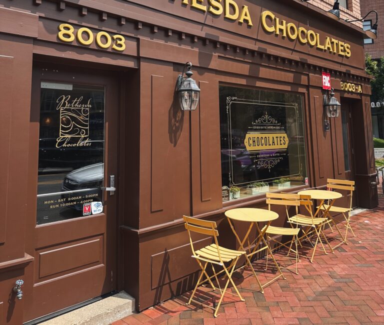 Exterior of Bethesda Chocolates on Woodmont Avenue in downtown Bethesda with yellow cafe tables and chairs.