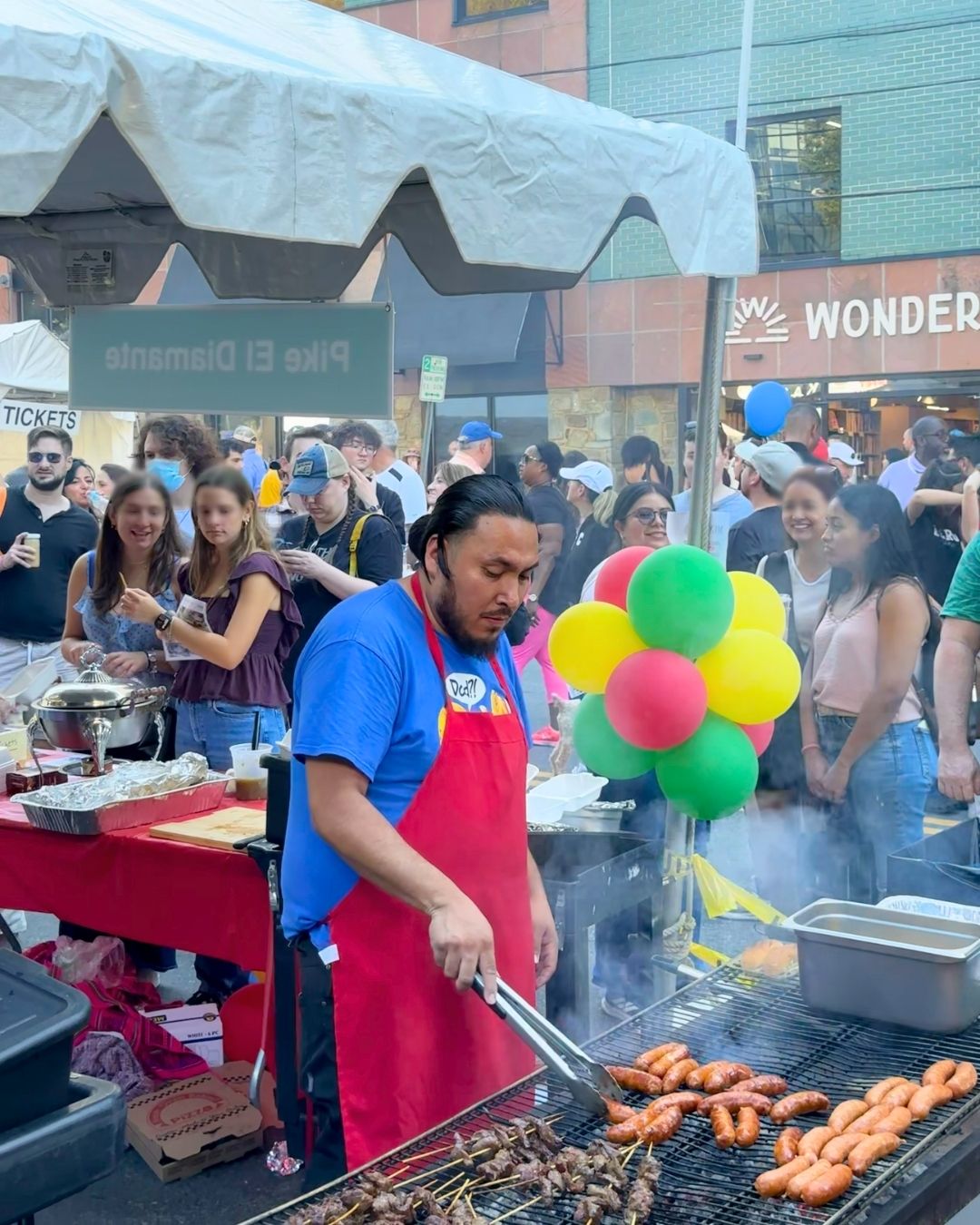 Grilled sausages and meat skewers cooking on outdoor grill at Pike El Diamante stand