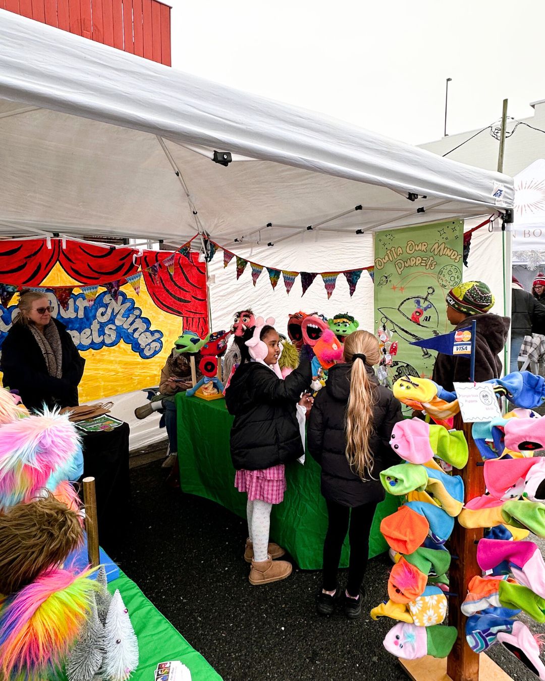 Kids reach for colorful puppets at vendor booth.