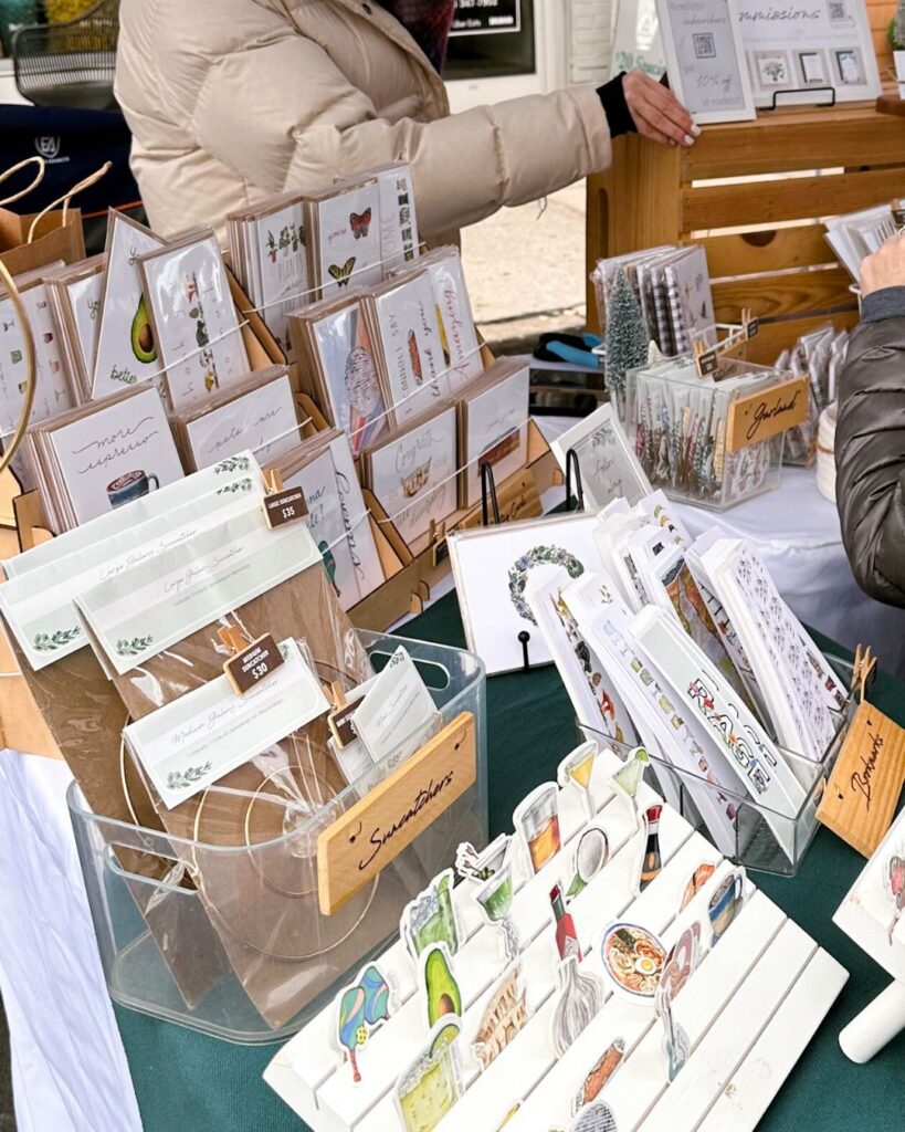 Close-up of stickers and small prints arranged at D Prince Designs vendor booth.