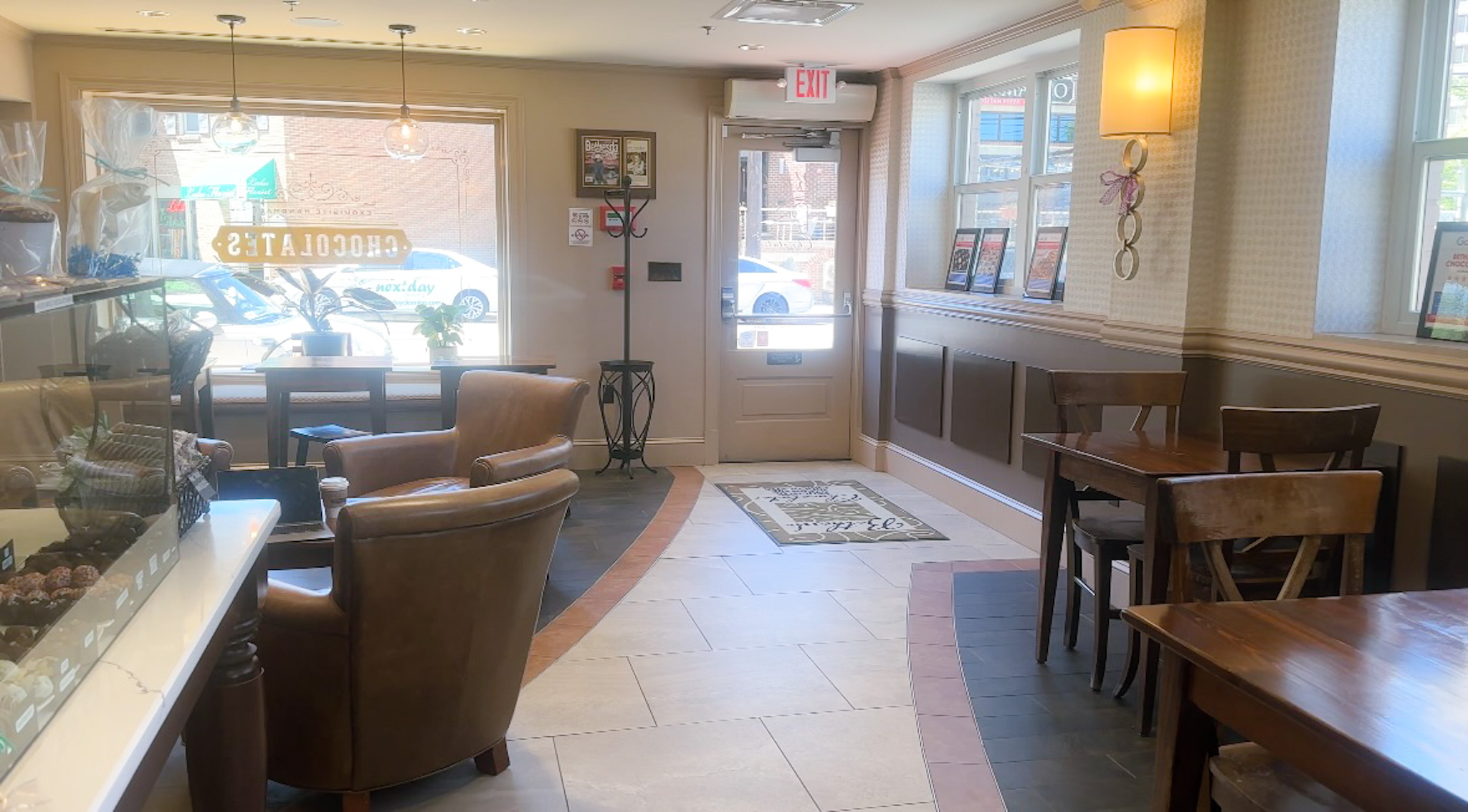 Window seating area inside Bethesda Chocolates with brown leather armchairs and cafe tables, and a view of Woodmont Avenue.