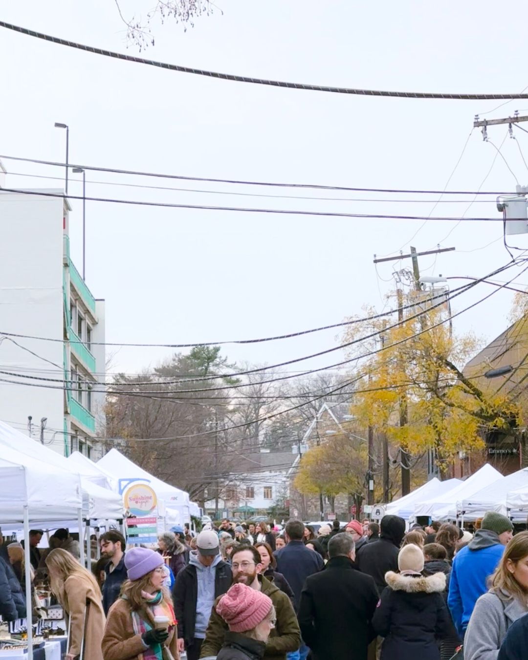 Wide view of market tents and bundled up shoppers sipping hot drinks.