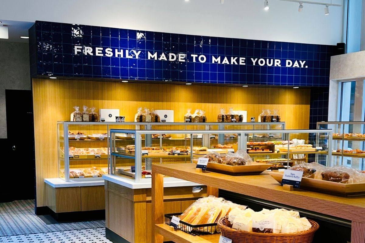 Wood display shelves with blue tile wall reading "FRESHLY MADE TO MAKE YOUR DAY" at Paris Baguette in Bethesda