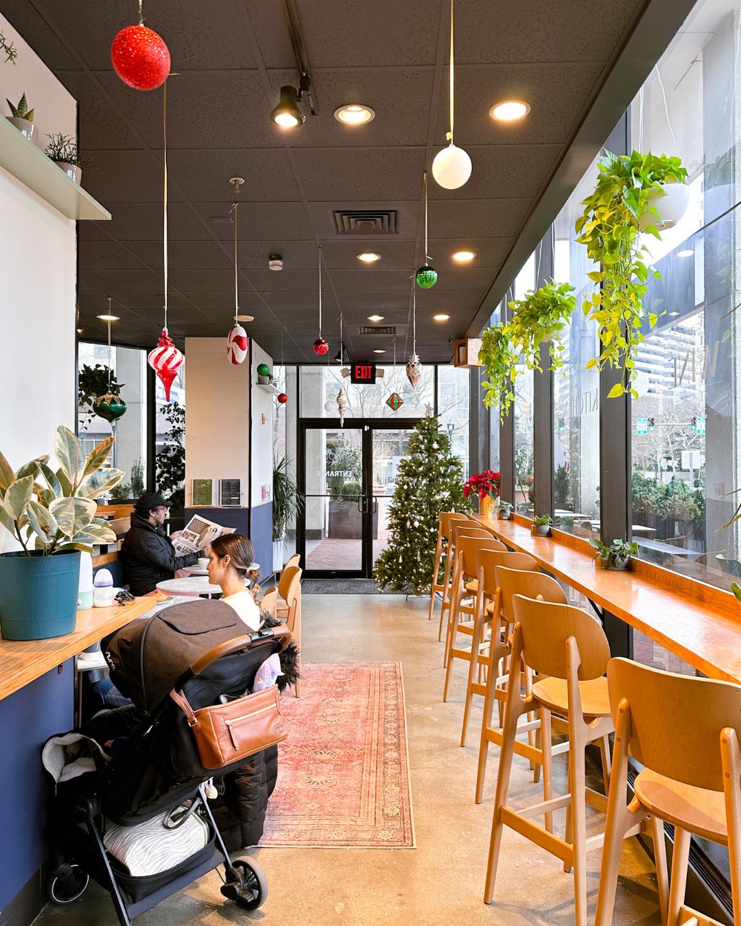 Interior of Simon Cafe Bethesda with customers at tables, floor-to-ceiling windows, wooden communal seating, and hanging holiday ornaments
