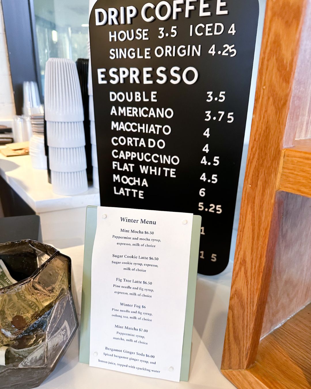 Coffee menu board at Bethesda’s Simona cafe showing drip coffee and espresso drink prices, with winter seasonal menu card featuring specialty lattes and drinks