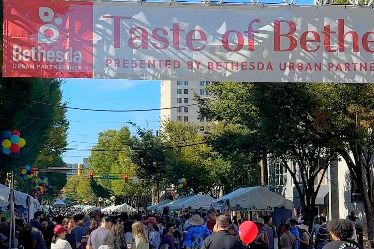 Large Taste of Bethesda banner stretched across busy festival street with crowds below