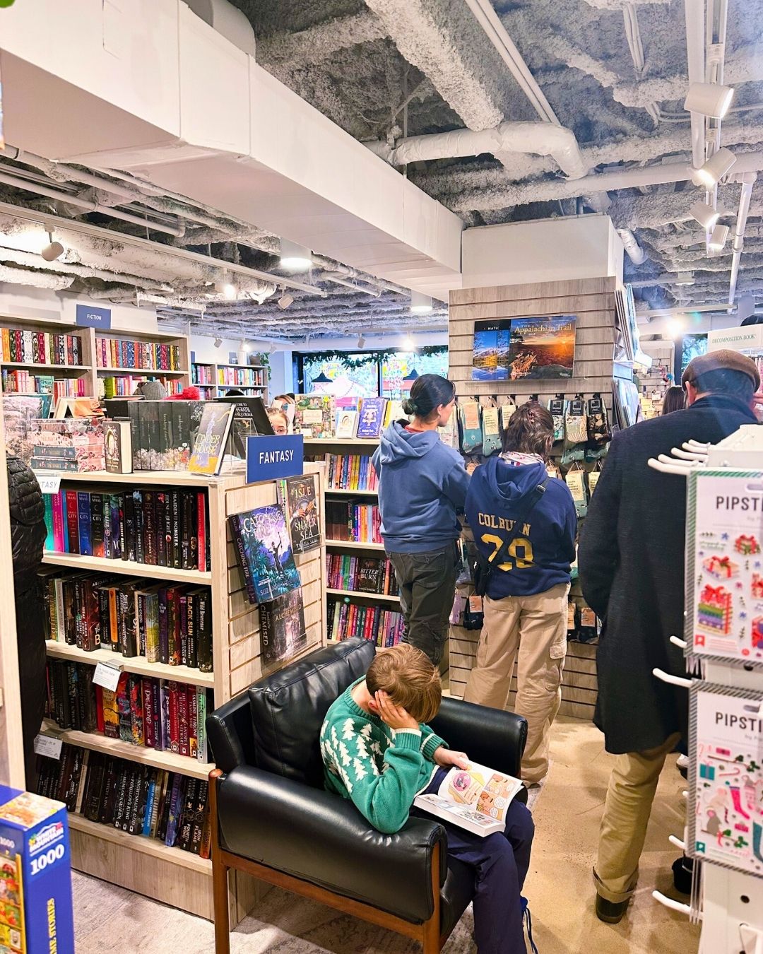 A young boy on a black leather seat reading next to folks in line at checkout